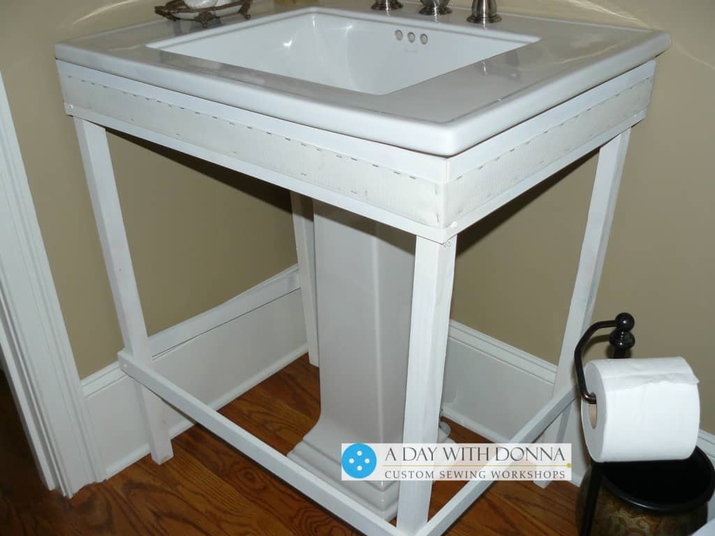 Make a frame from lumber to fit under the lip of the sink. Attach Velcro hook along the sides and front of the frame. This will hold your skirt to the frame.